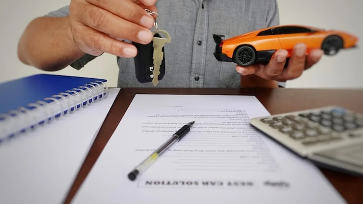 Mężczyzna trzymający klucz do zapłonu i mały samochód na papierze umowy