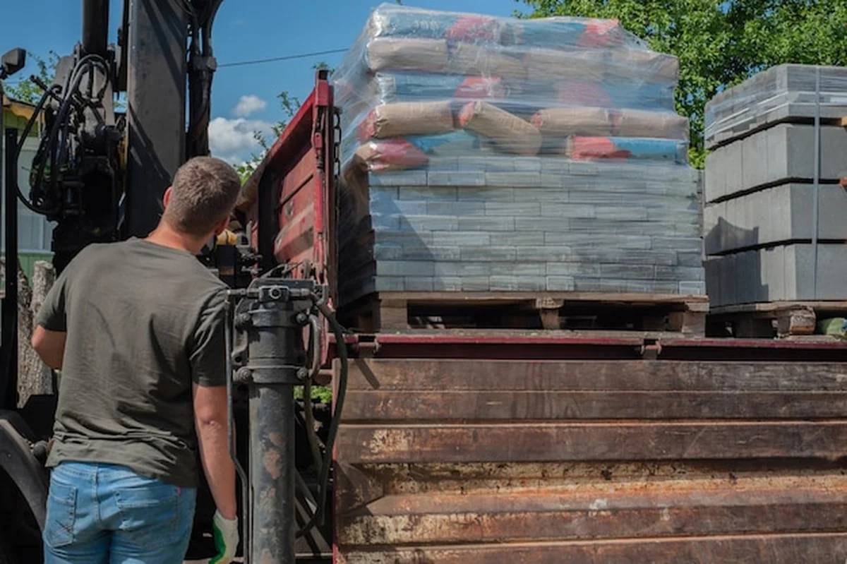 Rozładunek płyt chodnikowych z ciężarówki przez pracowników i manipulator