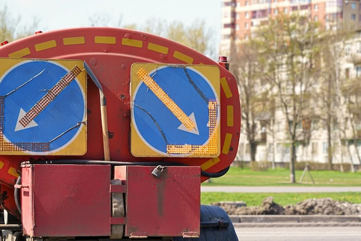 Czerwona ciężarówka z niebieskimi i żółtymi znakami na drodze