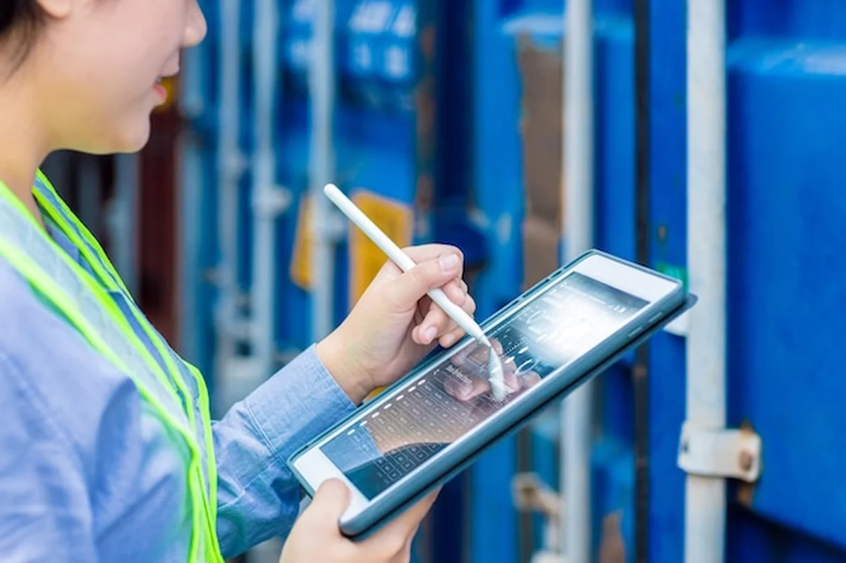 Pracownik logistyczny z tabletem i aplikacją do śledzenia kontenerów towarowych