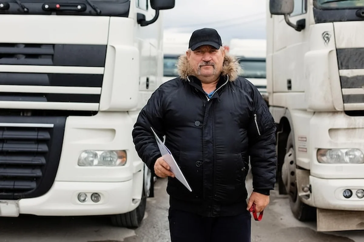 Mężczyzna kierowca ciężarówki trzyma dokumenty do załadunku na tle innych ciężarówek