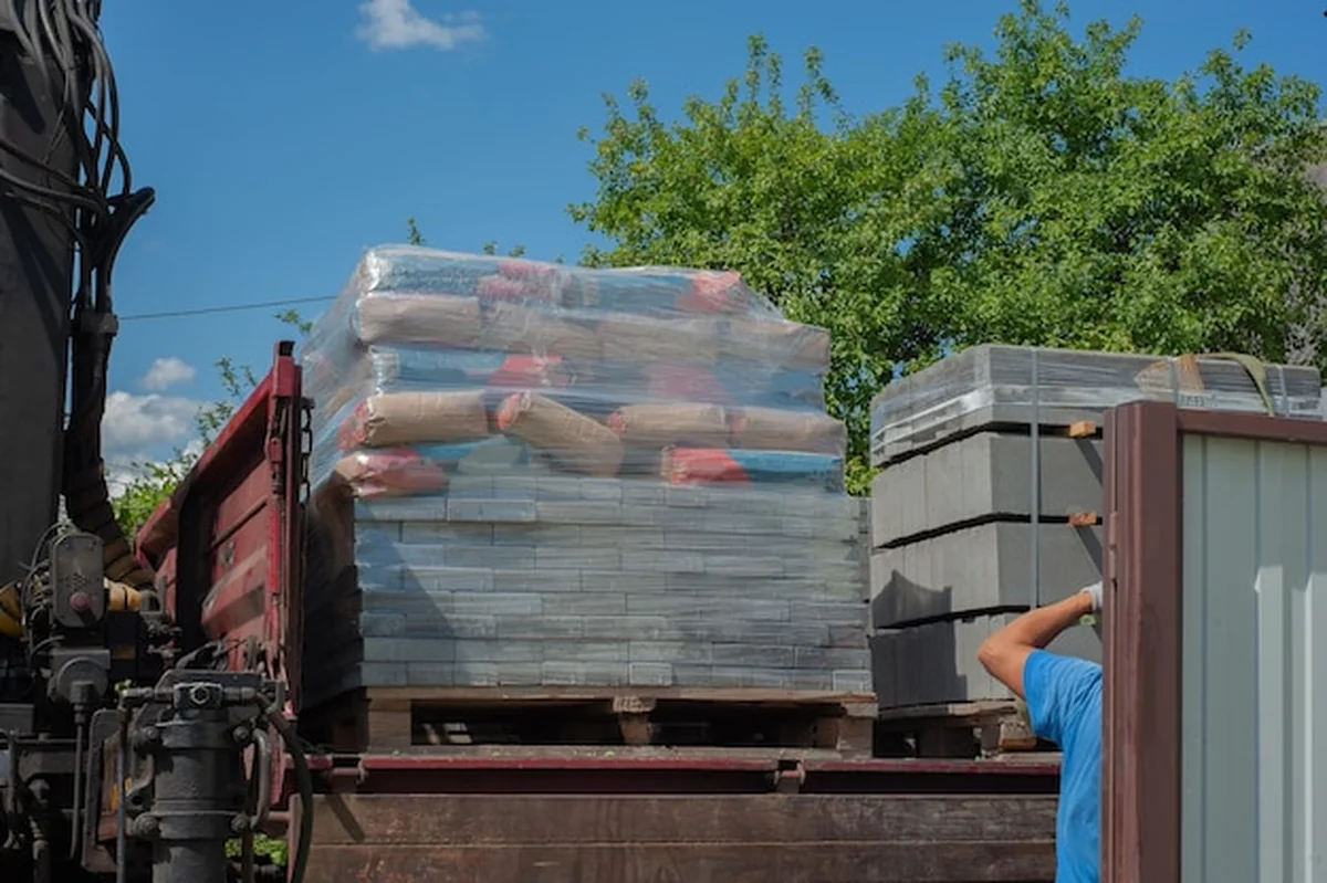 Rozładunek płyt chodnikowych z ciężarówki przez pracowników za pomocą manipulatora